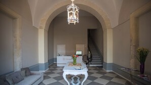 A lobby with a checkered floor, a white sofa, a glass coffee table, a chandelier, a reception desk, and a staircase.