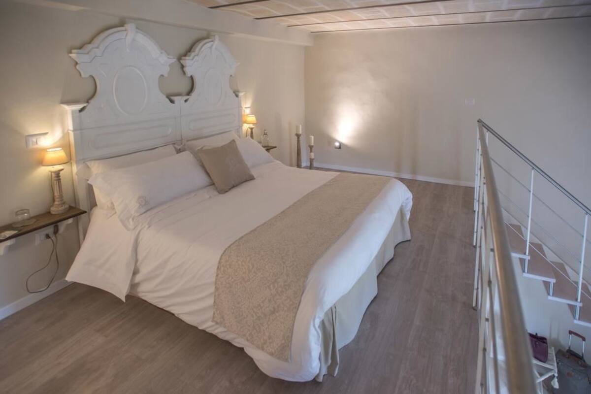 Una cama bien tendida con un cabecero blanco, una colcha color beige y dos lámparas de noche.