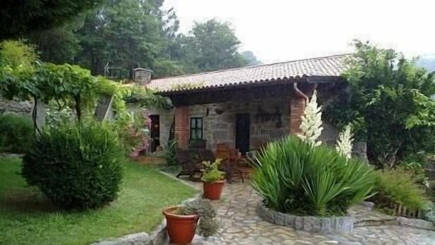A stone pathway leading to a rustic stone building with a tiled roof, surrounded by lush greenery and potted plants. - Casal de Folgueiras (Meis)