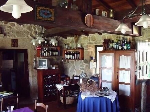 A rustic interior with stone walls, wooden beams, and a bar area with wine bottles. - Casal de Folgueiras (Meis)