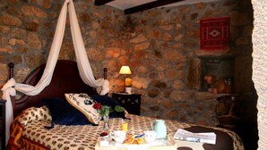A room with a stone wall, a bed with a canopy, a nightstand with a lamp, and a tray with breakfast items. - Casal de Folgueiras (Meis)