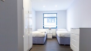 A modern, well-lit hotel room with two beds, a nightstand, a dresser, and a window with blinds. - Access Tower Hill (London)