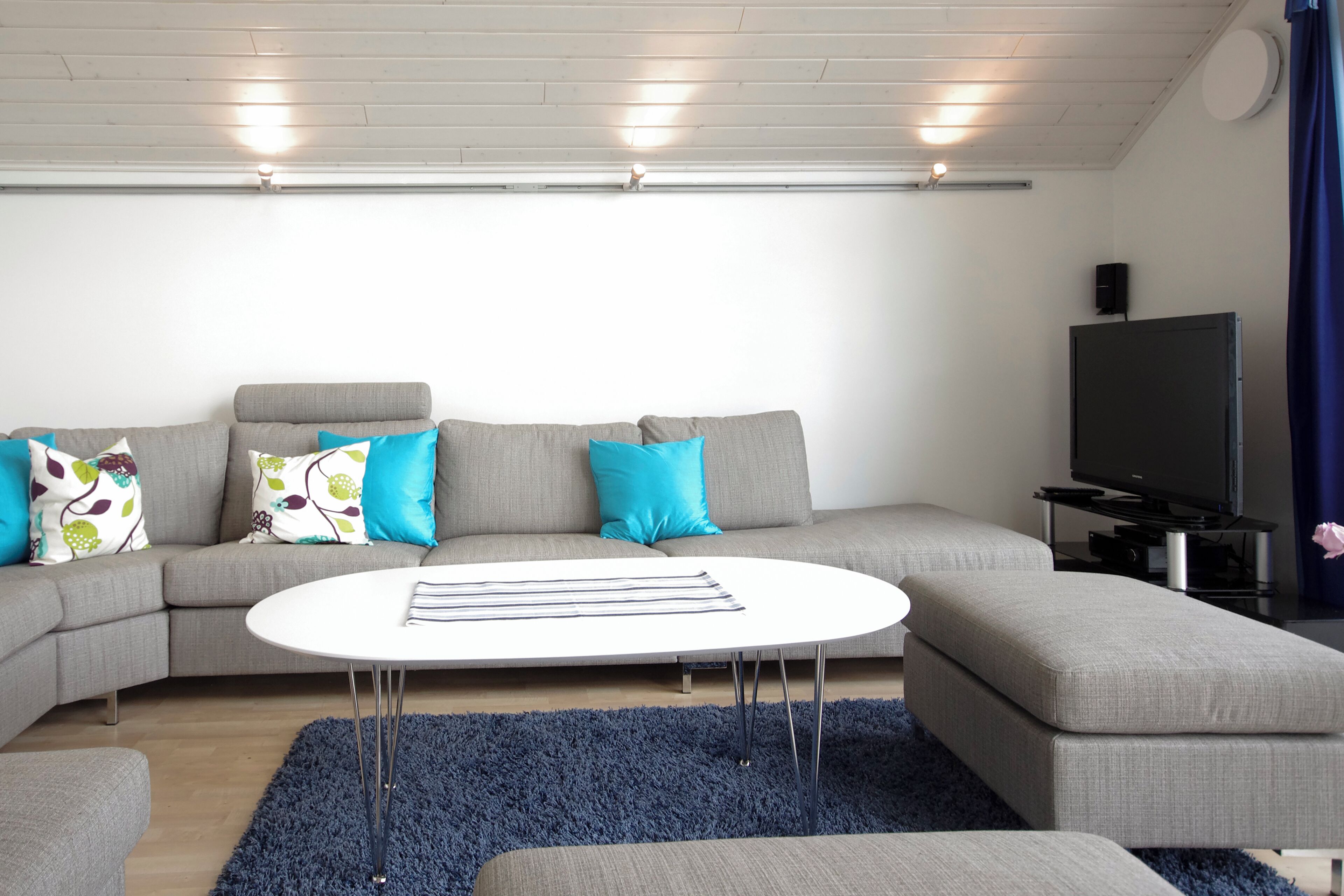 A modern living room with a grey sectional sofa, a white coffee table, and a flat-screen TV.