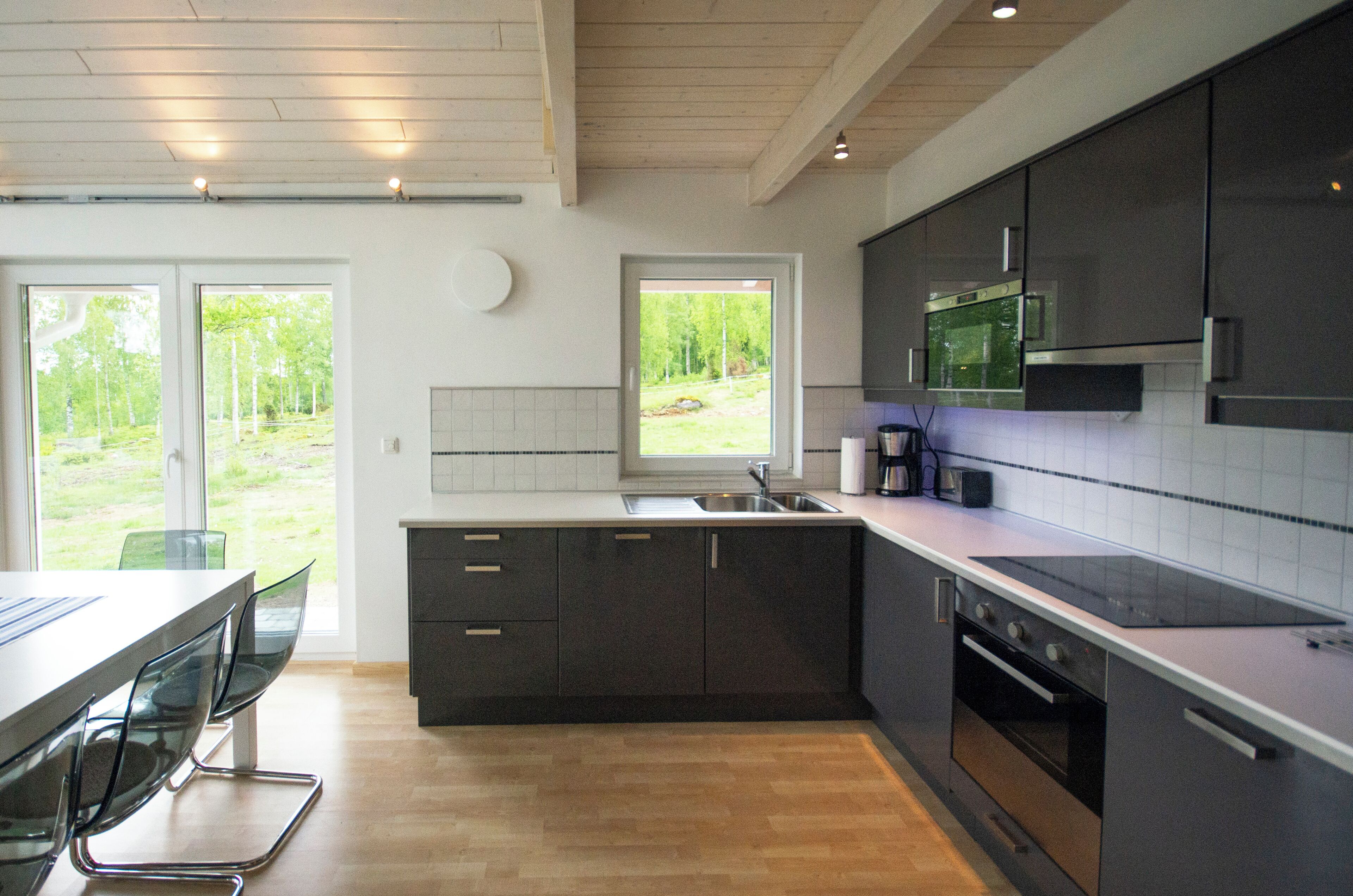 Een moderne keuken met donkere kastjes, een roestvrijstalen spoelbak en een ingebouwde oven. Een groot raam biedt uitzicht op de omgeving.