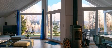A modern living room with a fireplace, large windows, and a dining area.