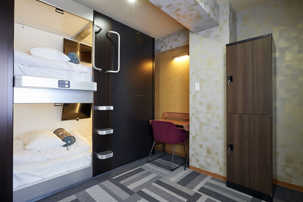 Una habitación de hotel compacta con literas, un escritorio y un armario.