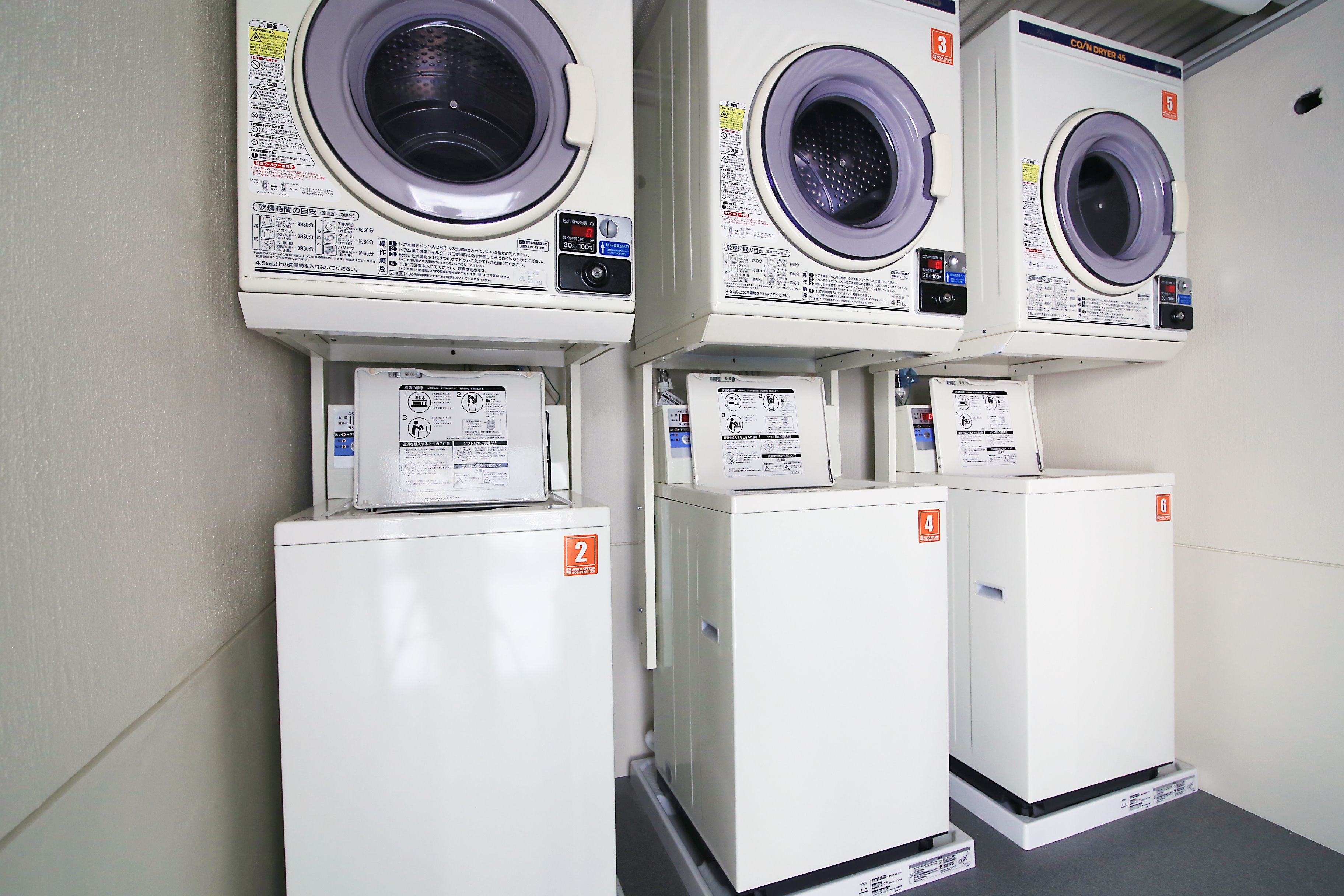 A row of stacked washing machines and dryers in a commercial setting.