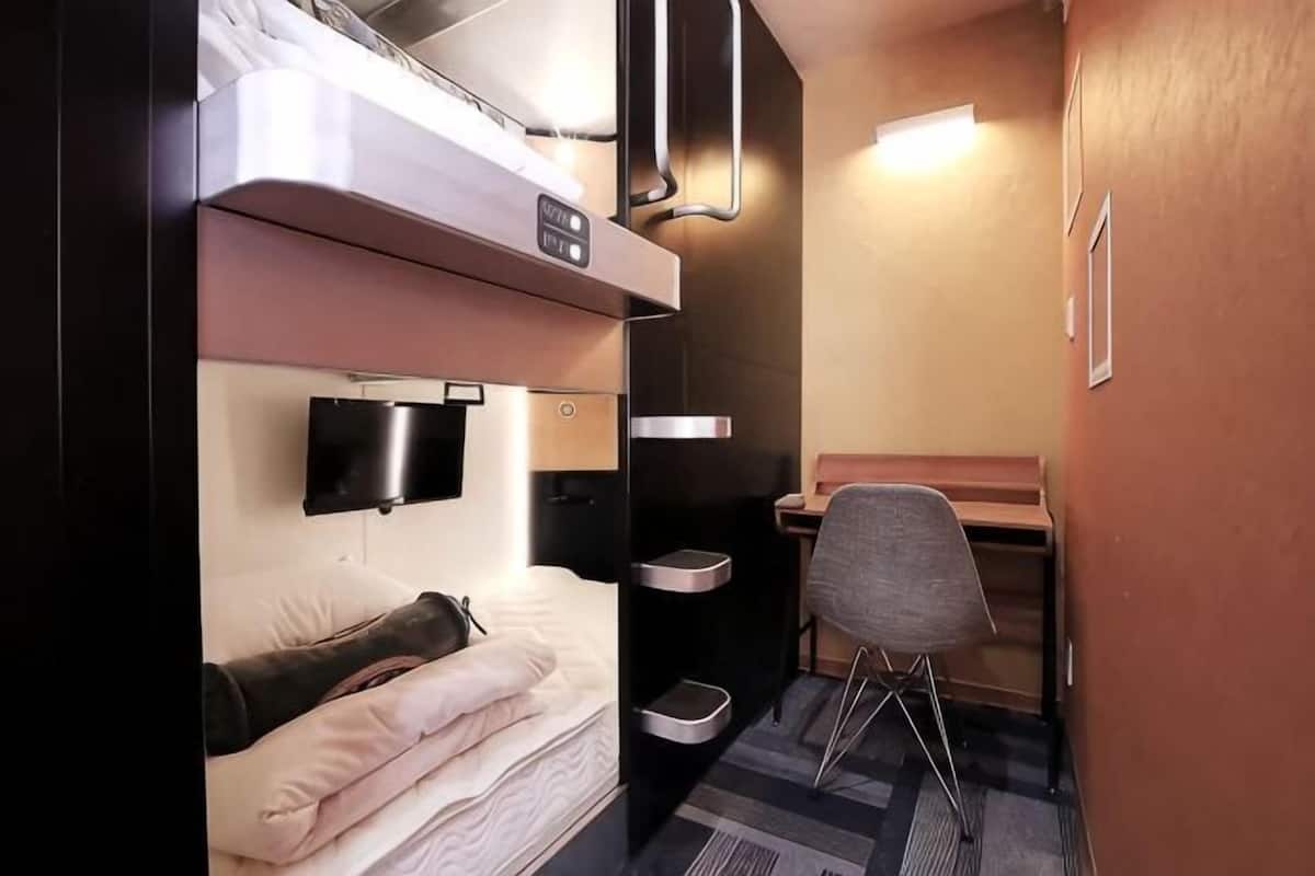 Una habitación de hotel compacta con literas, un escritorio, una silla, un televisor y una pequeña mesa.