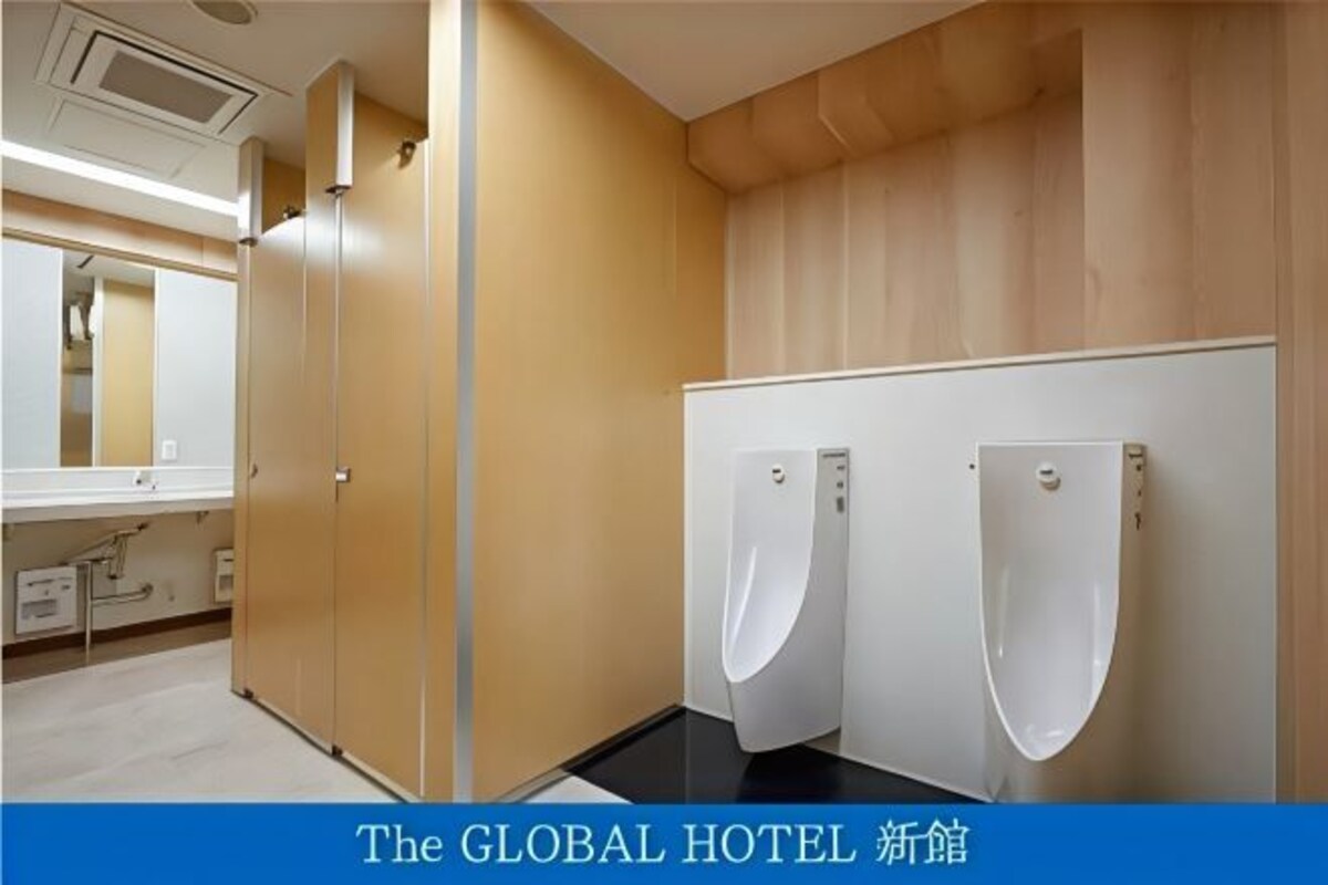 Des toilettes d’hôtel avec deux urinoirs, un miroir et un lavabo.