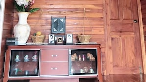 Una habitación con paneles de madera, un ventilador de techo, un aparador de vidrio con objetos decorativos y dos cuadros en la pared.