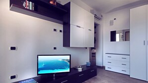A modern living room with a flat-screen TV, a bookshelf, and built-in cabinets. - Rena Bianca Suite (Santa Teresa di Gallura)