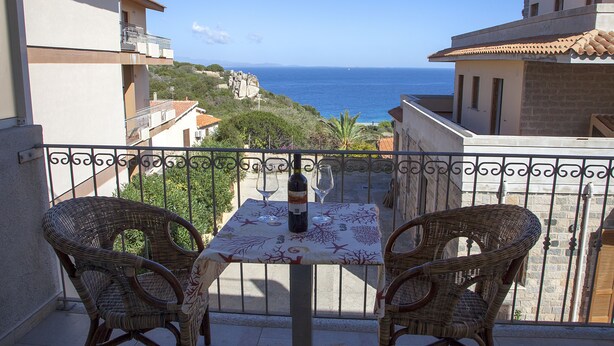 A balcony with wicker chairs, a table with a bottle and wine glasses, and a view of the sea. - Rena Bianca Suite (Santa Teresa di Gallura)