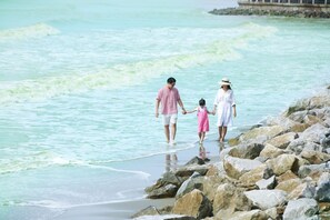 A family walking along a rocky shoreline with clear turquoise water. - FLC Grand Hotel Samson (Sam Son)