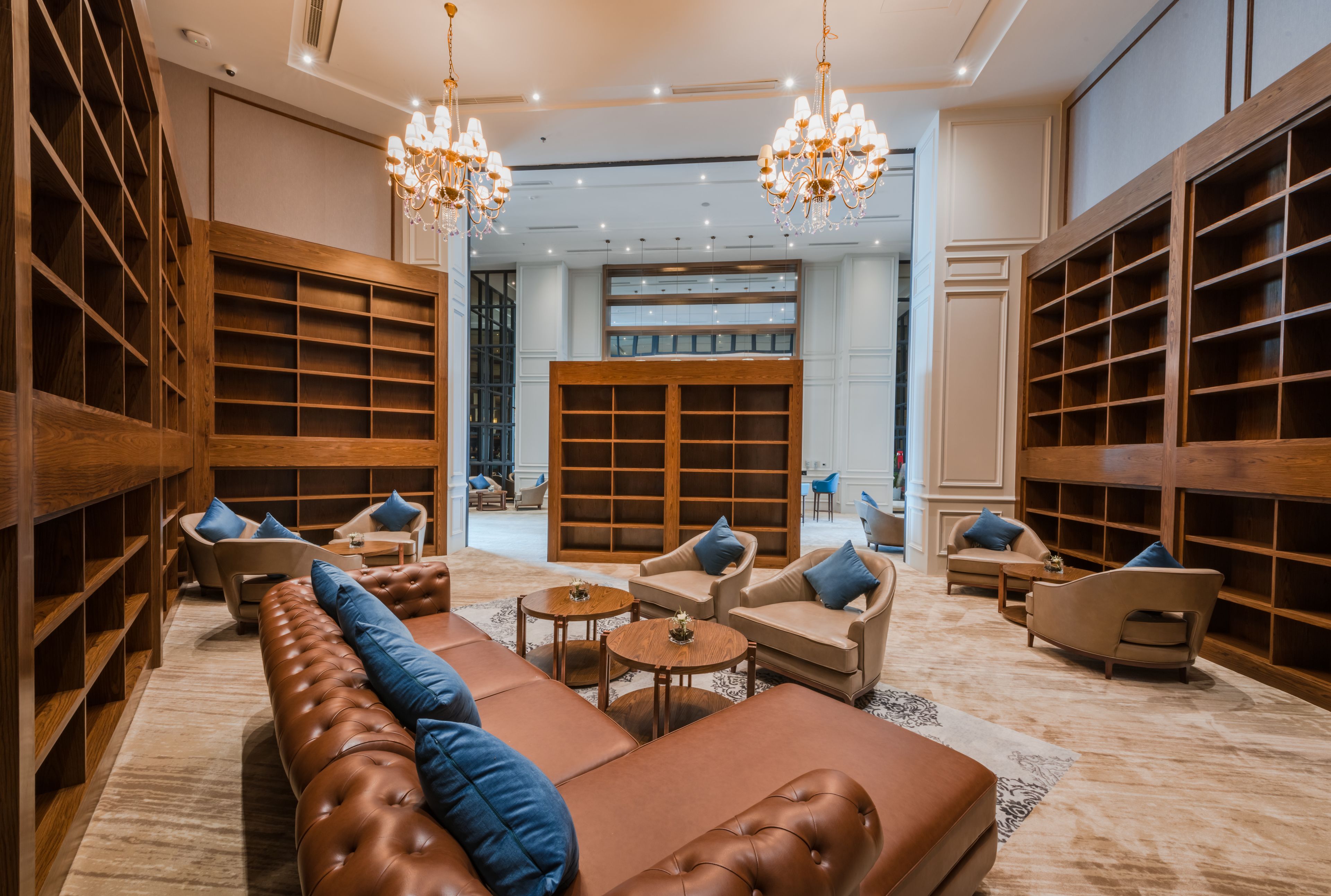 A spacious lounge area with leather sofas, wooden bookshelves, and a chandelier.