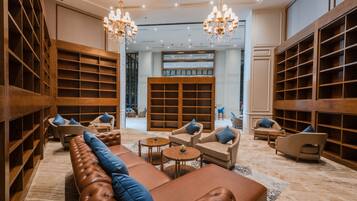 A spacious lounge area with leather sofas, wooden bookshelves, and a chandelier.