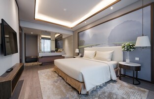Una habitación de hotel moderna con una cama grande, televisor, baño con espejo y un cuadro en la pared.
