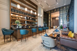A bar area with multiple stools and a bar counter, a seating area with sofas and chairs, and a large window providing natural light.