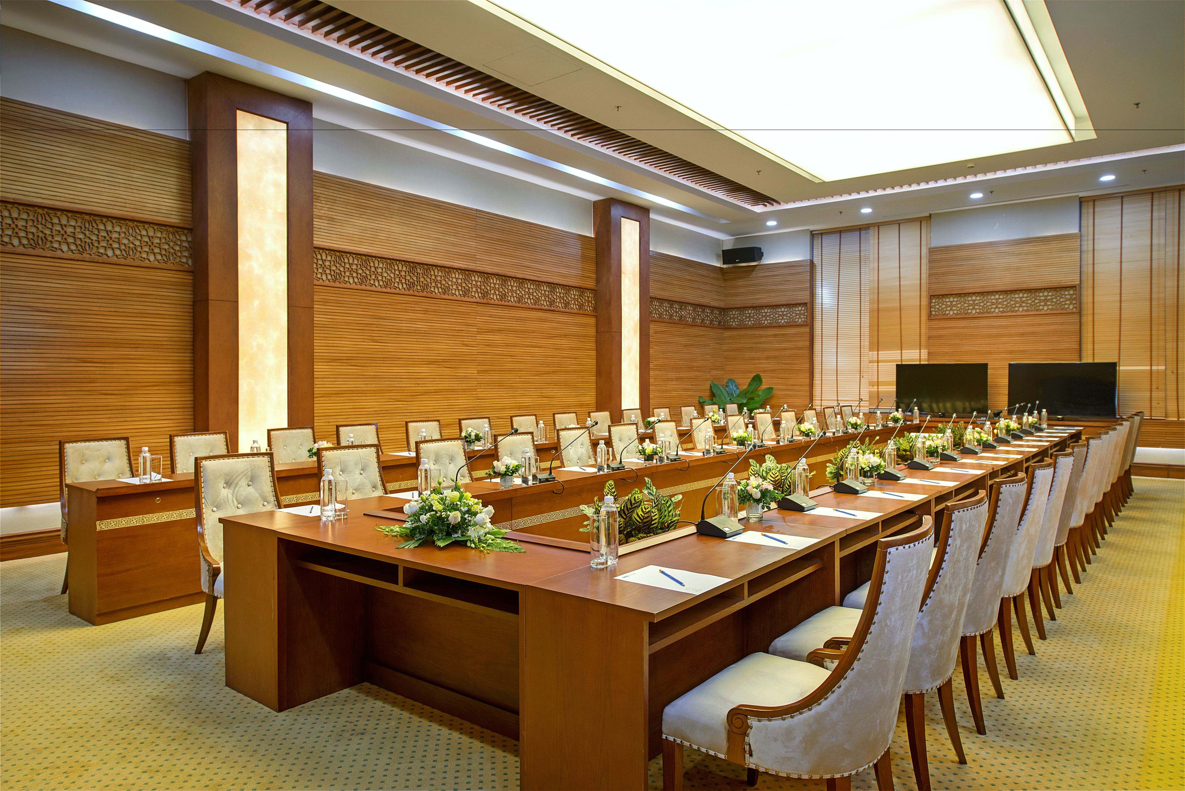 Un salón de conferencias con una larga mesa, sillas y una pantalla de televisión.