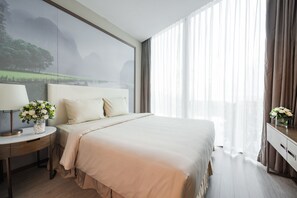 A modern hotel room with a large bed, a nightstand with a lamp, and a view of a misty landscape through sheer curtains. - FLC Grand Hotel Samson (Sam Son)