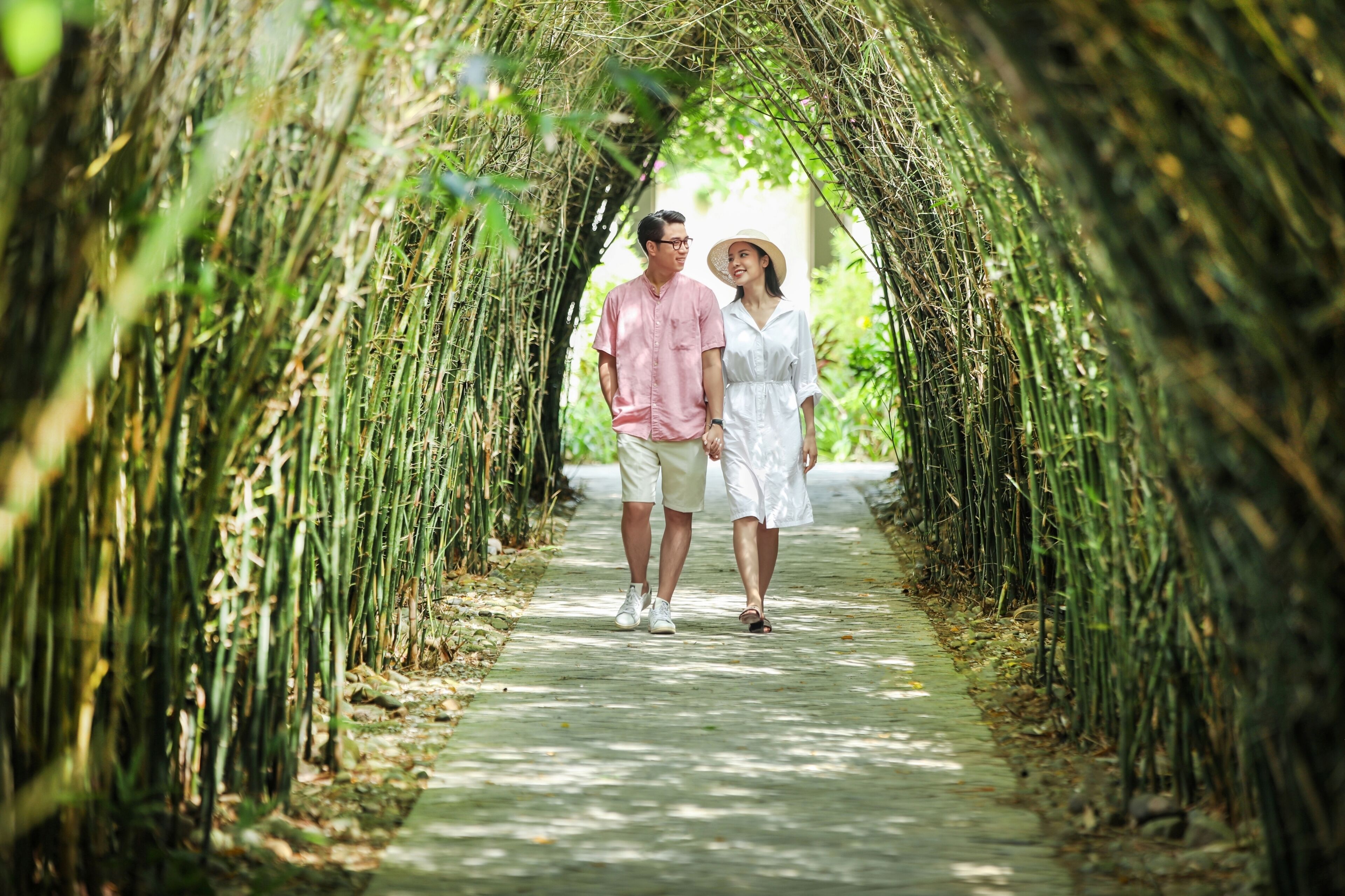 A couple walking through a bamboo tunnel pathway.
