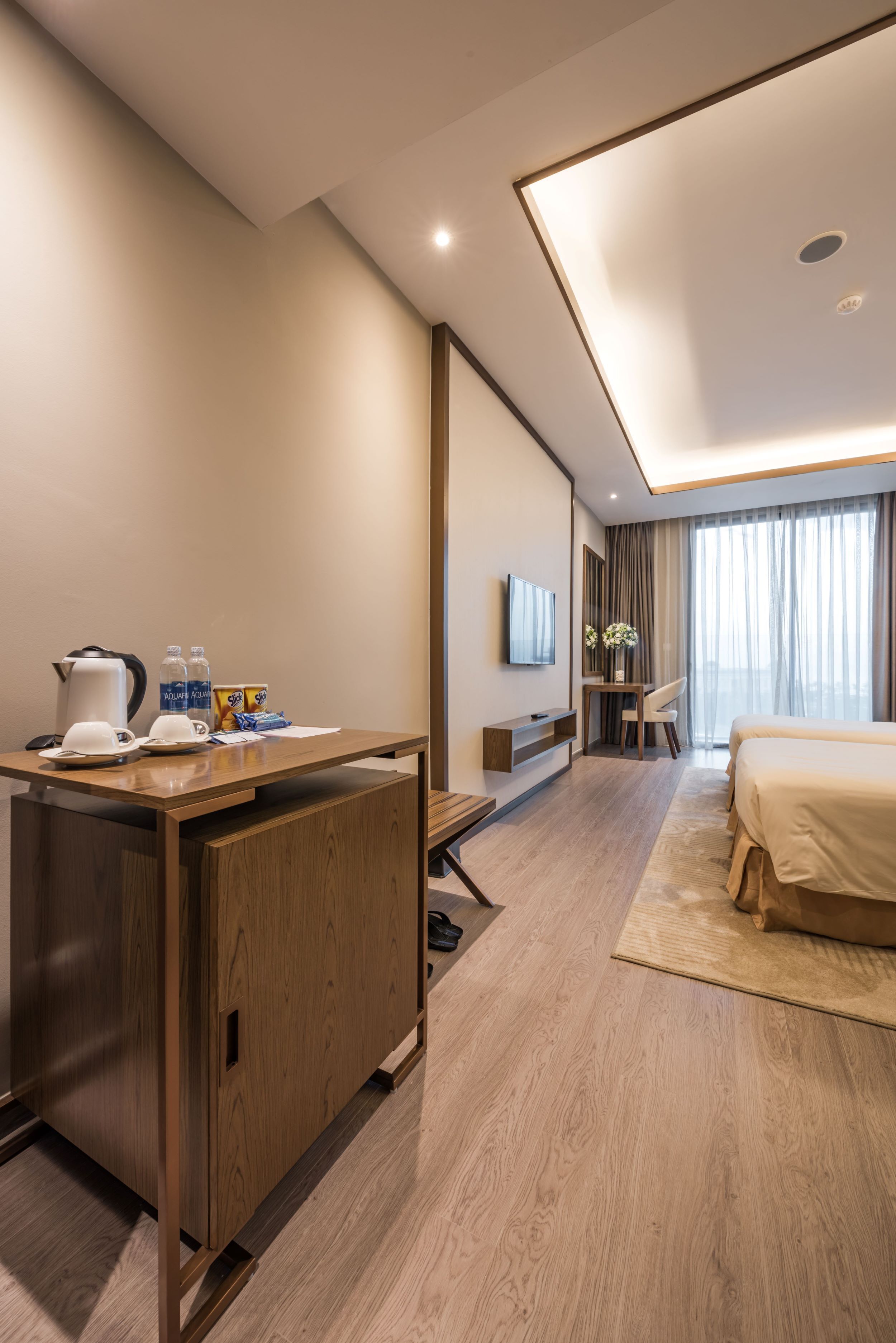 A modern hotel room with a wooden desk, a bed, a TV, and a large window with curtains.