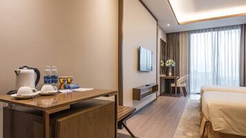 A modern hotel room with a wooden desk, a bed, a TV, and a large window with curtains.