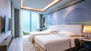 A hotel room with two beds, a TV, a desk, and a large window with a view of the sea. - FLC Grand Hotel Samson (Sam Son)