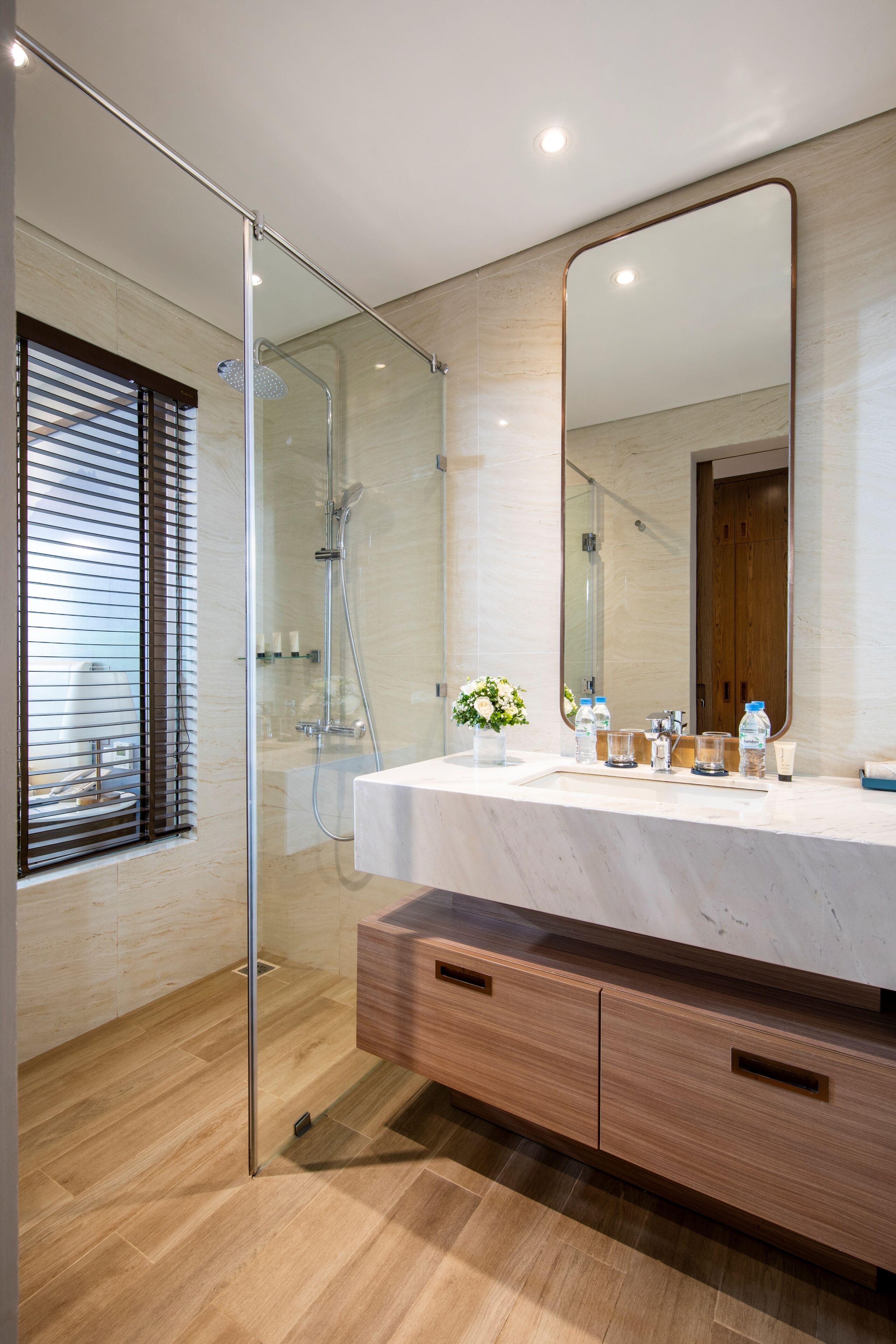 Een moderne badkamer met een douchekabinet van glas, een grote spiegel en een houten wastafelmeubel met lades.