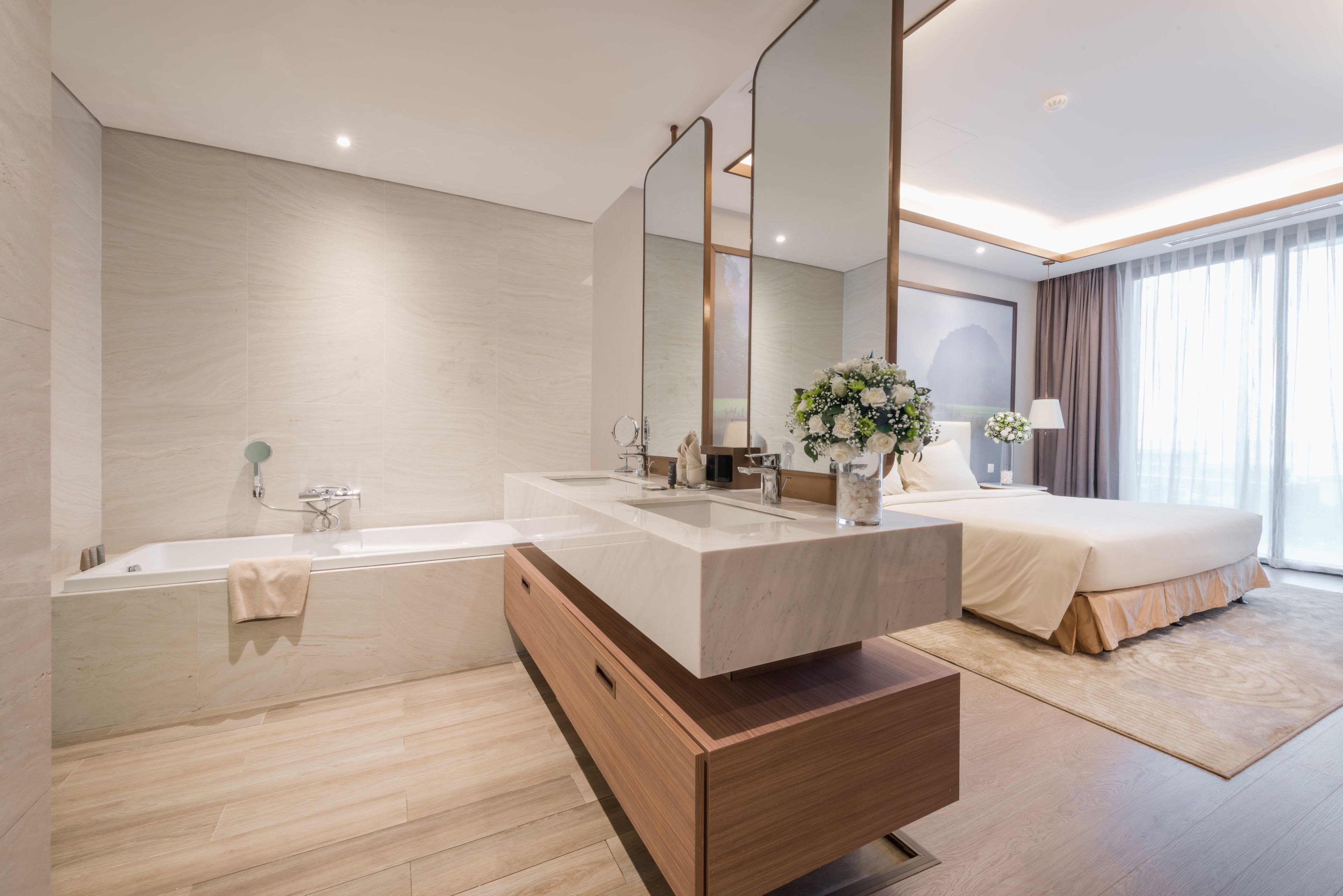 A modern hotel bathroom with a large bathtub, a double sink vanity, and a large mirror.