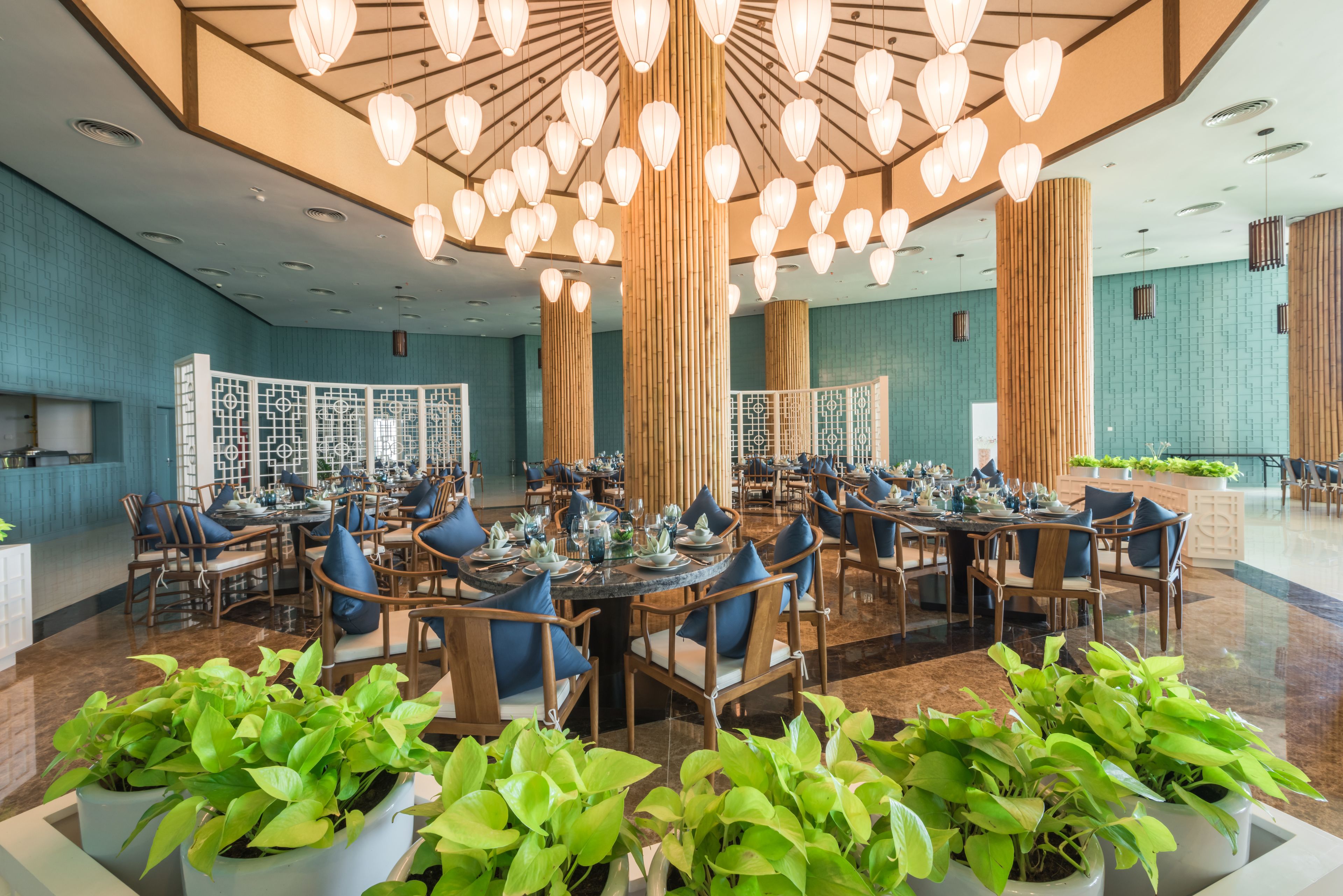 A spacious dining area with multiple tables and chairs, large wooden columns, and hanging lantern-style lights.