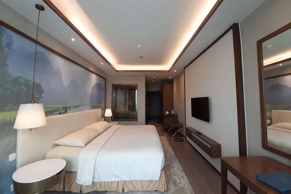 A modern hotel room with a large bed, bedside lamps, a round table, a TV, and a mural on the wall.