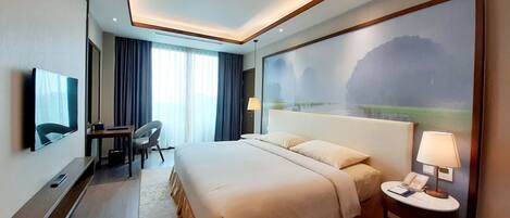 A hotel room with a large bed, a desk, a chair, a TV, and a painting of a landscape.