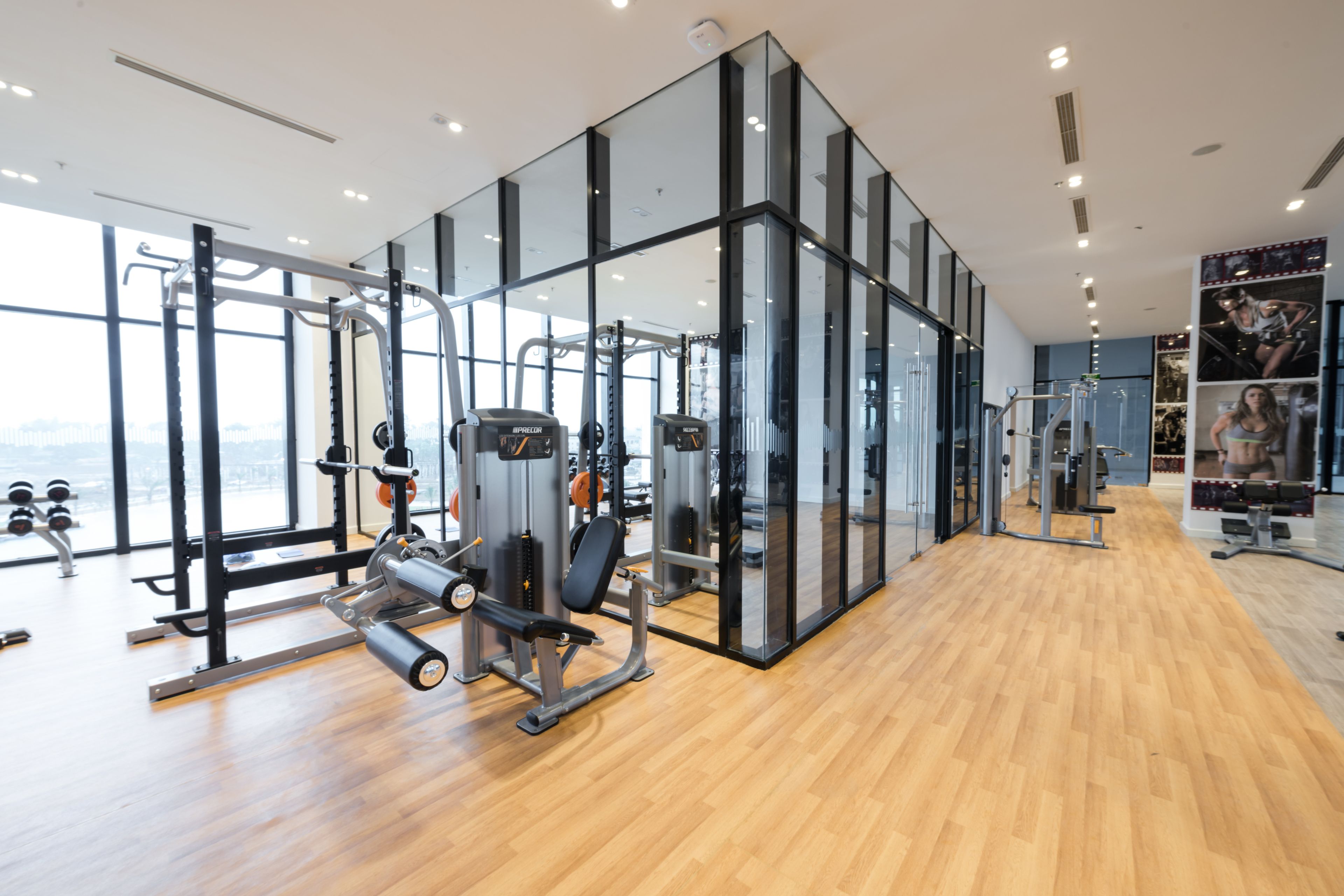 Une salle de sport moderne équipée de divers appareils d’exercice, dotée de grandes fenêtres et d’un plancher en bois.