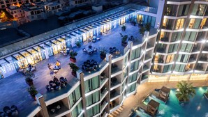 A rooftop terrace with outdoor seating, a swimming pool, and a glass-enclosed building. - FLC Grand Hotel Samson (Sam Son)