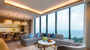 A modern living room with a large sofa, a coffee table, and a dining area with chairs and a table. - FLC Grand Hotel Samson (Sam Son)