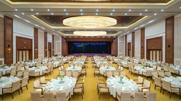 A large banquet hall with round tables, chairs, and a stage at the front.