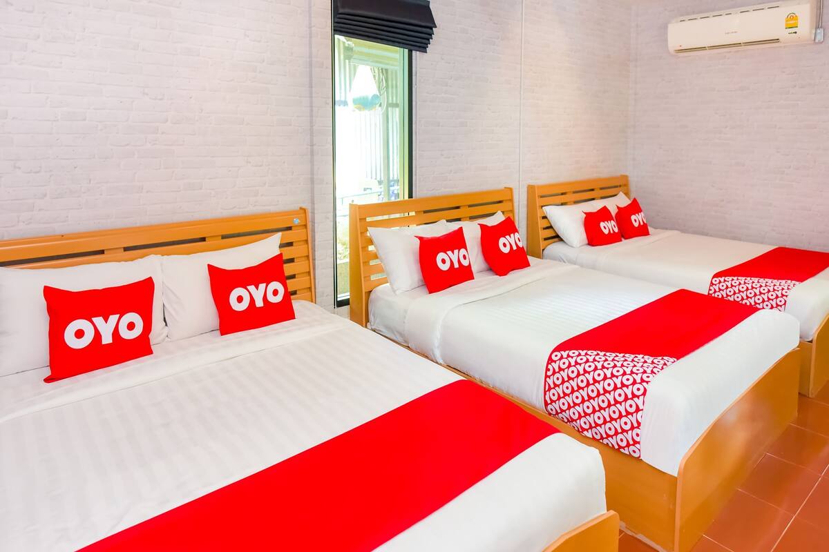 Une chambre d’hôtel avec trois lits, chacun agrémenté de draps blancs et de touches de couleur rouge, notamment des oreillers et une couverture.