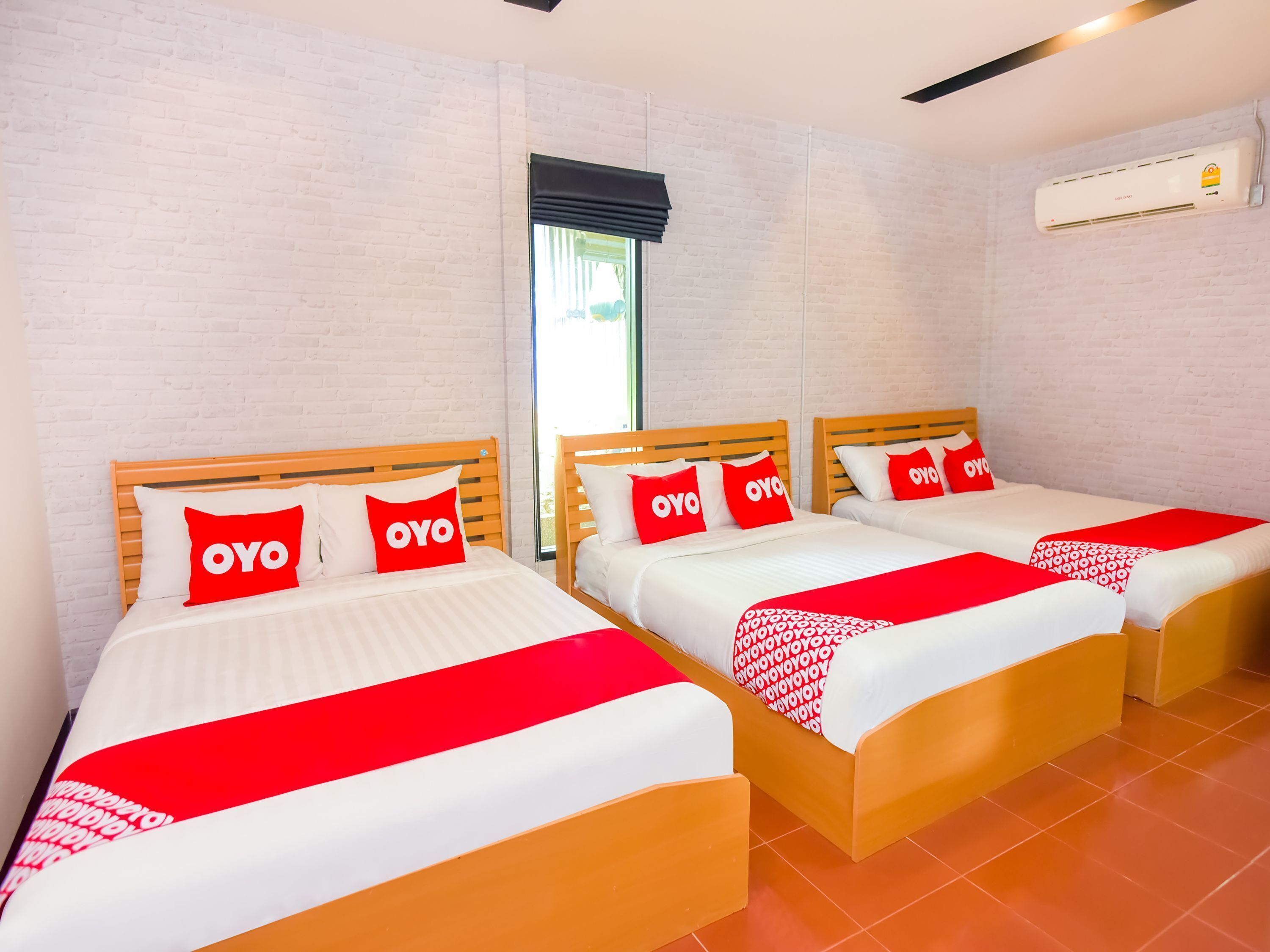 Habitación de hotel con tres camas, cada una con cubrecama y almohadas rojas y blancas que tienen la palabra 'OYO'.
