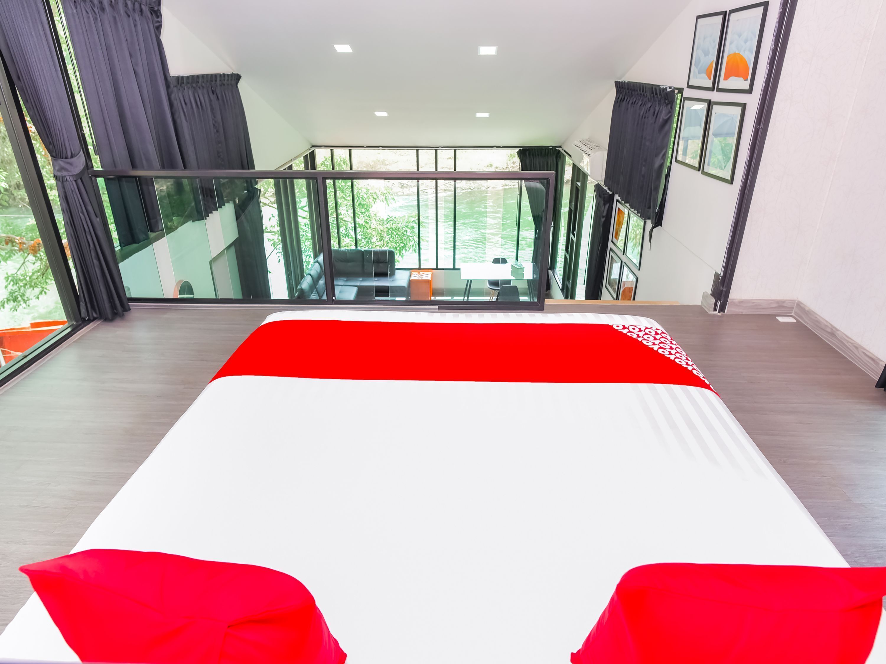Une chambre d’hôtel moderne dotée d’un grand lit, d’un balcon avec une rambarde en verre et offrant une vue sur la verdure environnante.