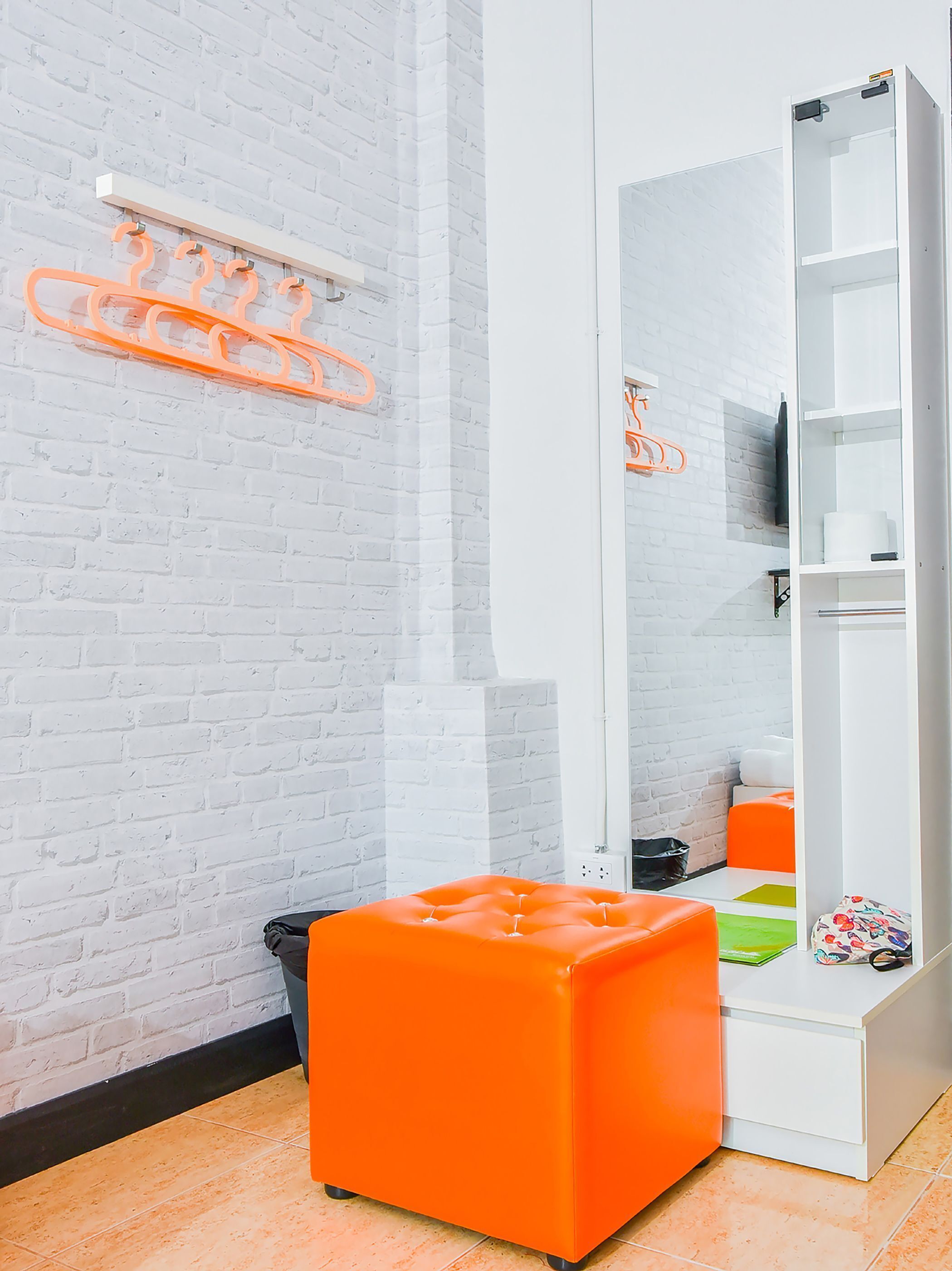 A room with a white brick wall, a white wardrobe, and an orange ottoman.