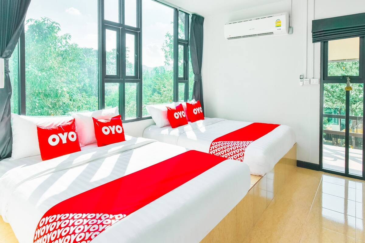 Une chambre d’hôtel avec deux lits, de grandes fenêtres, un appareil de climatisation et une vue sur la verdure.