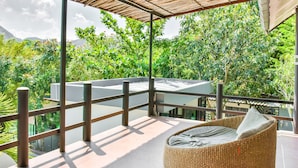 A balcony with a wicker chair, a glass railing, and a view of lush greenery and mountains. - Nana River Kaeng Krachan (Kaeng Krachan)