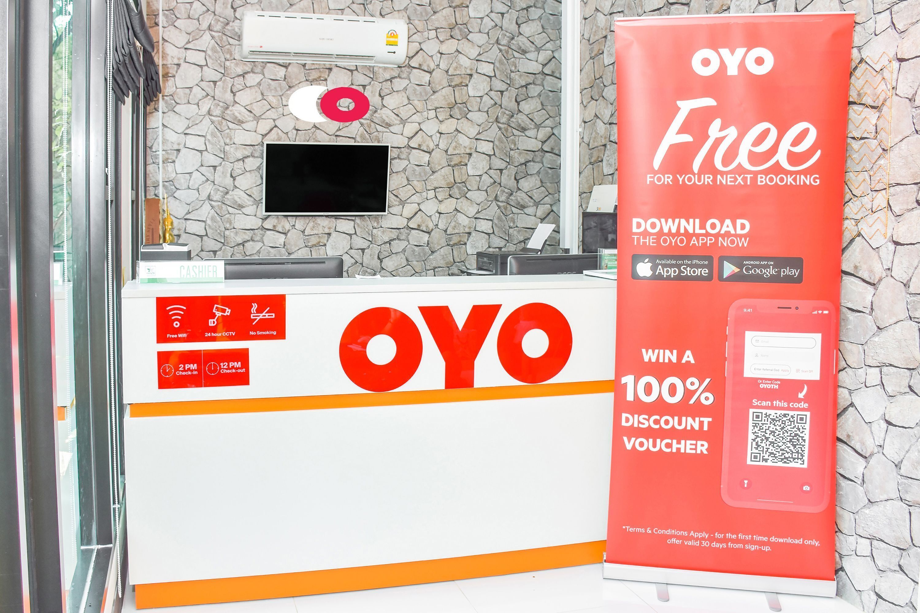 A reception desk with a large OYO sign, a digital screen, and a QR code for a discount voucher.