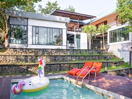 Uma casa moderna com piscina, paredes de pedra e cadeiras de lounge vermelhas.