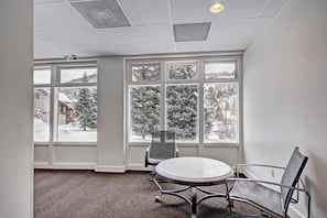 A conference room with a round table and two chairs, large windows with a snowy view, and a ceiling with recessed lighting. - Vs440h Village Square Hotel Room (Copper Mountain)