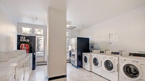 A laundry room with multiple washing machines, a refrigerator, and a window with a view of trees. - Vs440h Village Square Hotel Room (Copper Mountain)