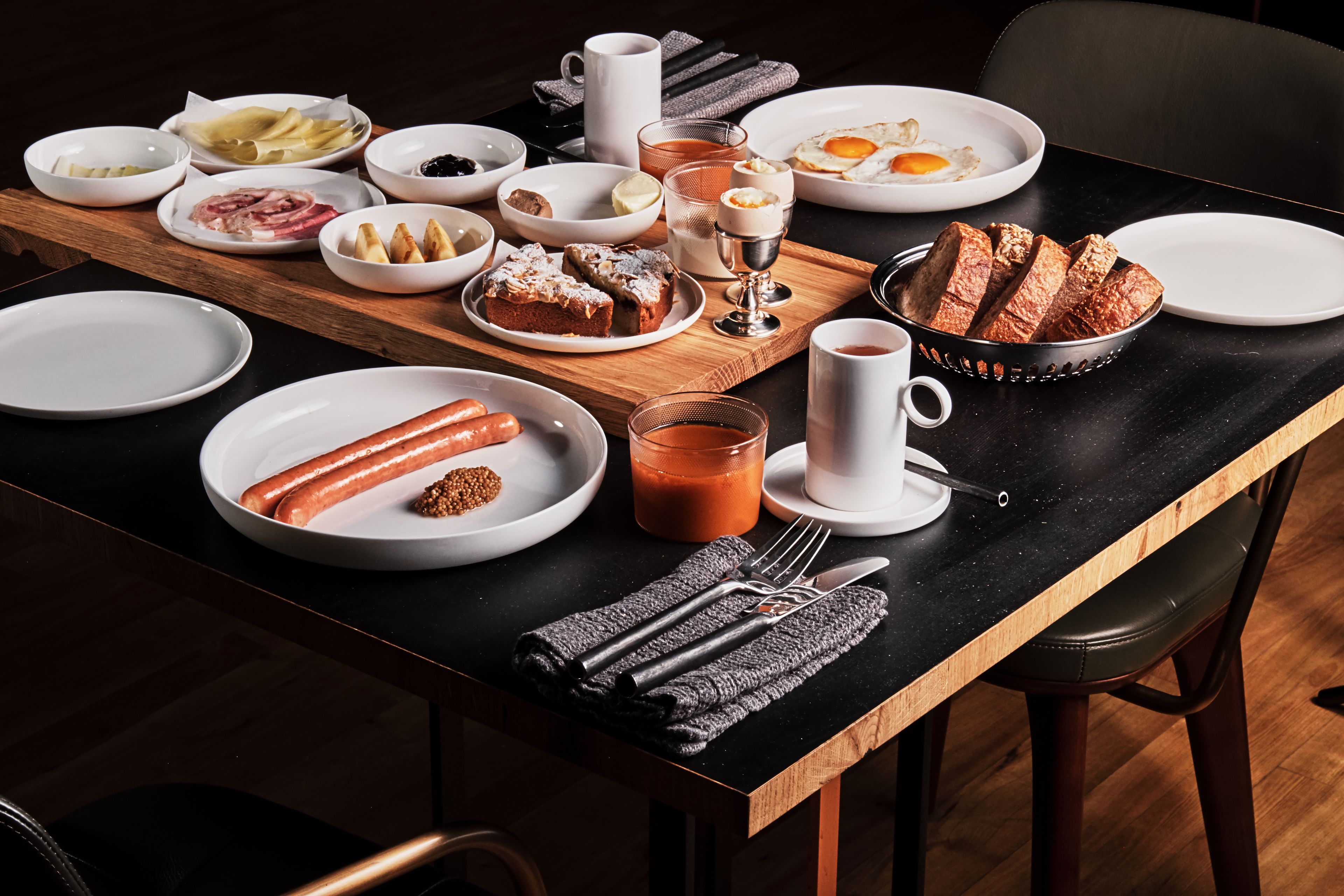 A breakfast table with various dishes, including sausages, pastries, and a coffee cup.