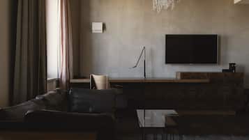 A modern living room with a leather sofa, a glass coffee table, a wooden side table, a flat-screen TV mounted on the wall, and a pendant light.