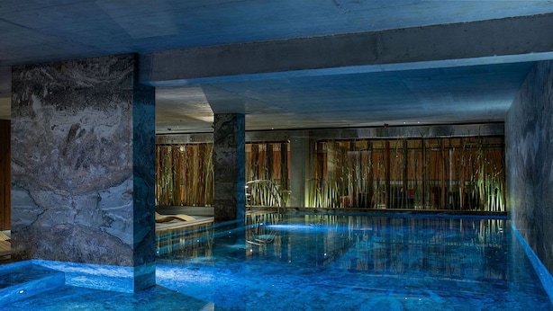 A modern indoor pool area with a glass enclosure, wooden seating, and bamboo decor. - Hotel Warszawa (Warsaw)