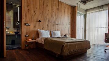 A modern bedroom with a wooden wall, a bed with white linens, a bedside table with a lamp, and a chair.